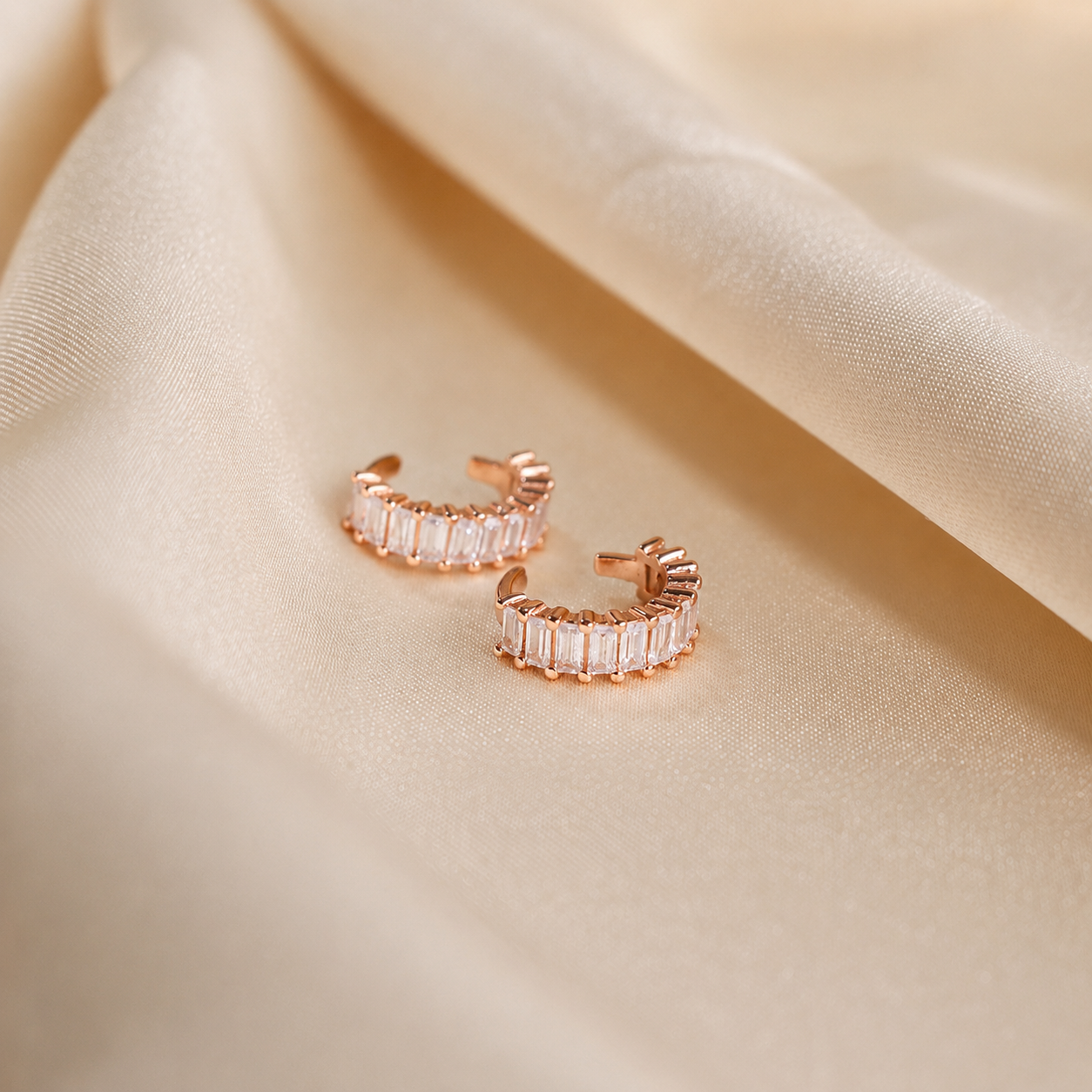 Rose gold hoop earrings with clear gemstones on a beige fabric background